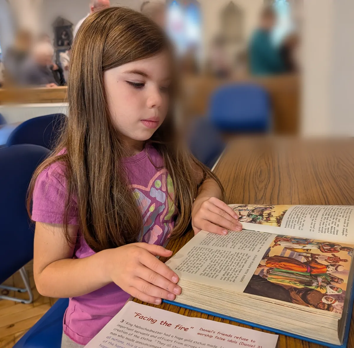 The sister at a table, reading a big picture book