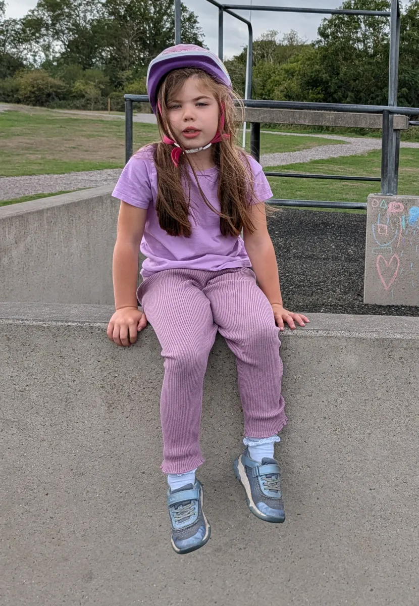 The sister in a cycle helmet, sitting on a low wall in a park