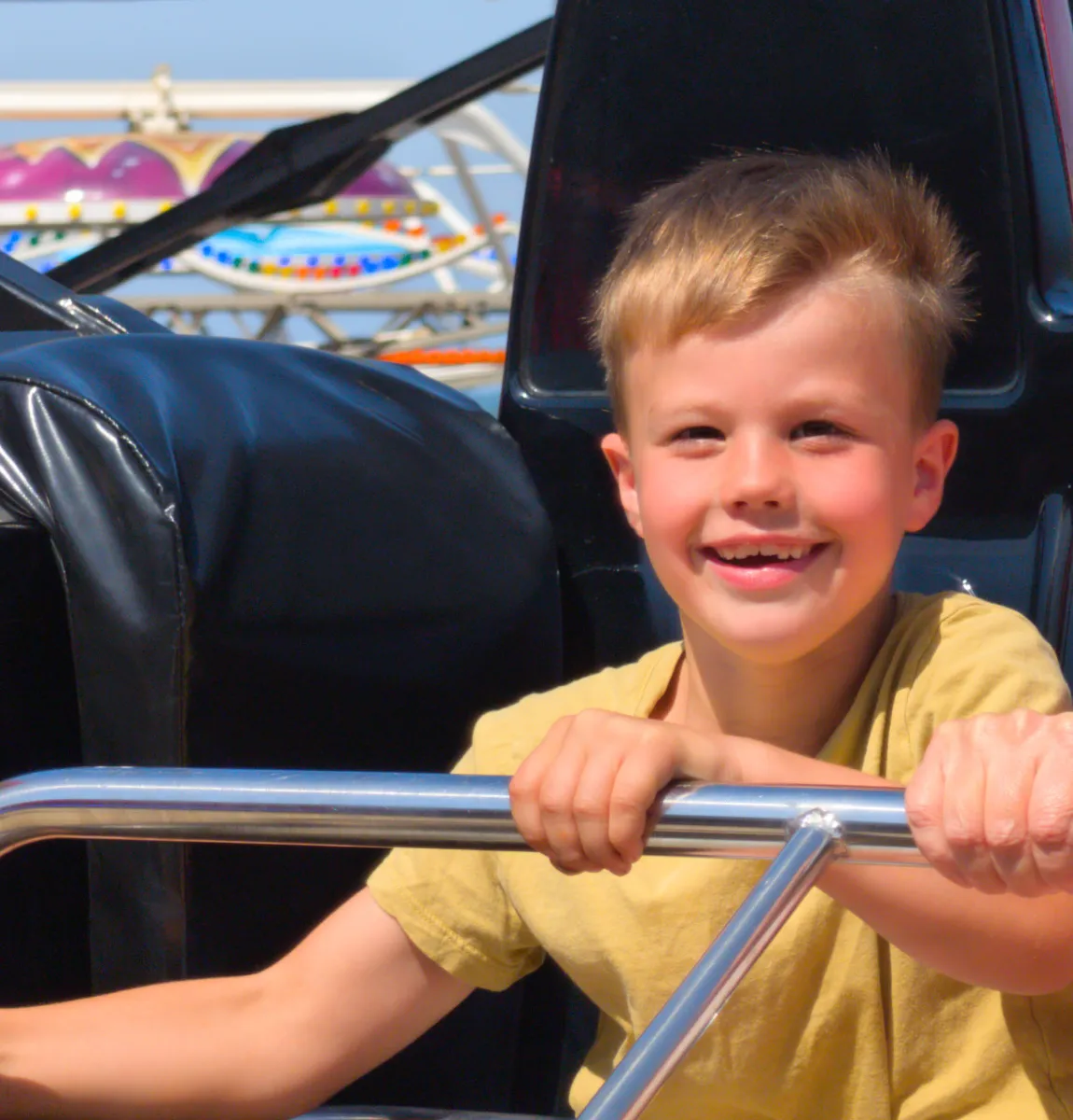 The brother grinning on a fairground ride, hands on the safety bar